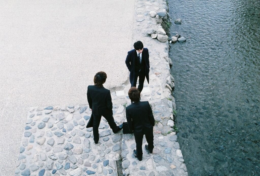 Three businessmen in suits stand by a river in Kyoto, Japan, engaged in discussion.